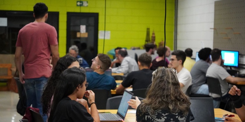 Fotografia colorida. Sala do Espaço Plasma da Unicamp, alunos da disciplina AM037 sentados nas mesas mexendo em computadores e debatendo. Fim da descrição.