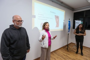 Foto colorida de equipe formada por duas mulheres e um homem fazendo uma apresentação para a classe. Fim da descrição.