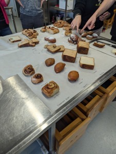 Foto colorida de mesa com produtos alimentícios da área de panificação e confeitaria feitos com os óleos desenvolvidos pela ÄIO Fim da descrição.