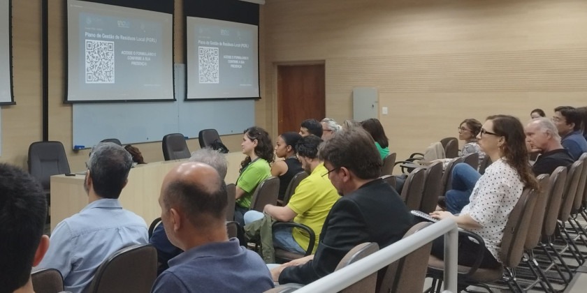 Participantes durante a apresentação do Plano de Gestão de Resíduos Local. Em segundo plano, apresentação sendo projetada Fim da descrição.