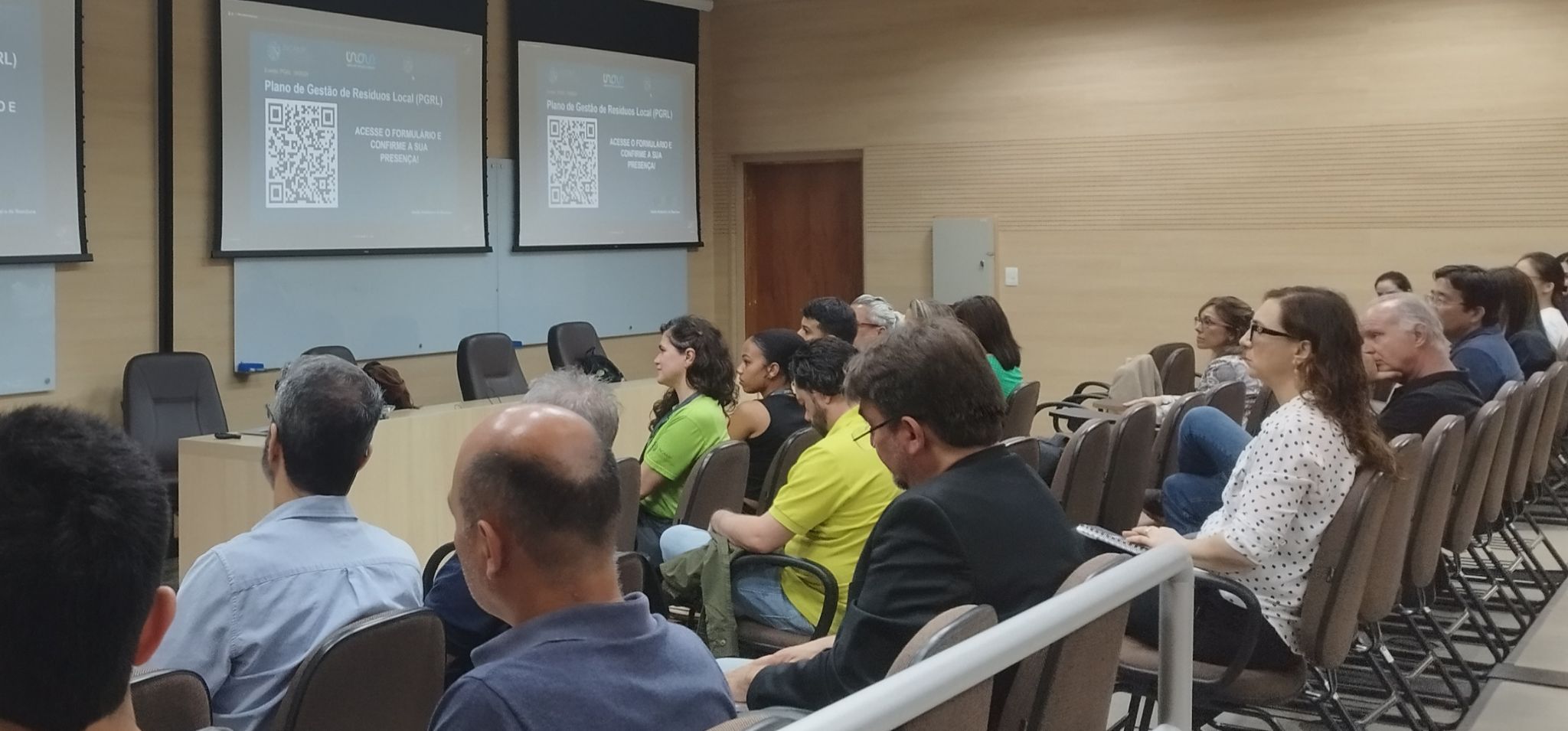 Participantes durante a apresentação do Plano de Gestão de Resíduos Local. Em segundo plano, apresentação sendo projetada Fim da descrição.