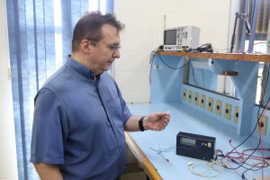 O professor Antônio Quevedo está em uma sala e segura uma agulha conectada a um aparelho eletrônico. Trata-se do protótipo do estimulador de nervo periférico, uma das tecnologias transferidas. Fim da descrição.