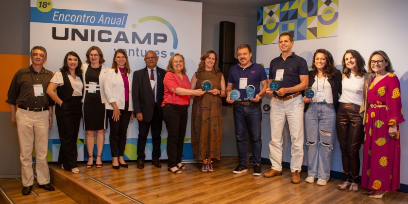 Fotografia colorida do momento em que vários empreendedores estão sendo premiados no Encontro Anual Unicamp Ventures. As pessoas estão em pé, uma ao lado da outra e olhando para a câmera sorrindo. Fim da descrição.