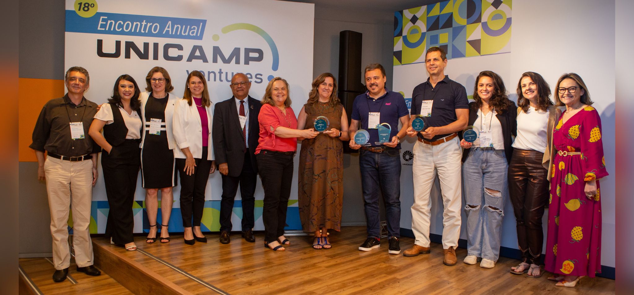 Fotografia colorida do momento em que vários empreendedores estão sendo premiados no Encontro Anual Unicamp Ventures. As pessoas estão em pé, uma ao lado da outra e olhando para a câmera sorrindo. Fim da descrição.