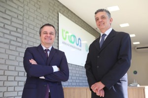 Os professores Rangel Arthur e Renato Lopes, diretores-executivos da Inova Unicamp. Rangel está a esquerda do vídeo com os braços cruzados e sorrindo. Renato está à direita com os braços estendidos. Ambos vestem terno e estão em uma sala com fundo de tijolos cinza e placa da Inova Unicamp. Fim da descrição.