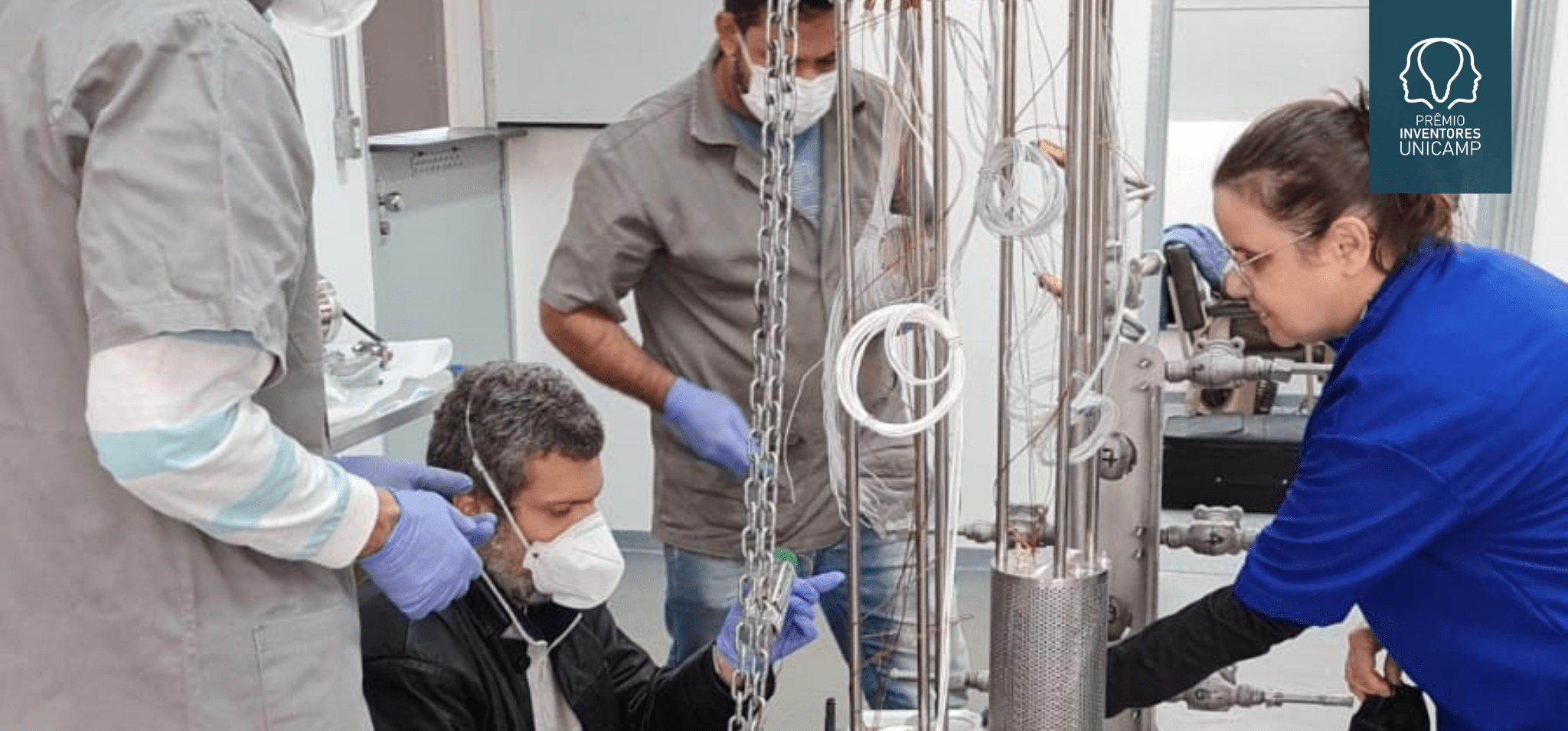 Criostato de argônio PULARC (Purification Liquid Argon Cryostat). Da esquerda para direita: os técnicos da Unicamp Gustavo Carrara, Frederico Demolin e Cezar Aguiar e a pesquisadora do CBPF Magda Fontes. Créditos: IFGW-Unicamp. Fim da descrição.