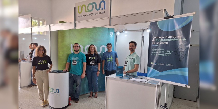 Estande e equipe da Inova Unicamp no evento Tecnologia em Foco. Fim da descrição.