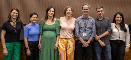 Fotografia colorida. Grupo de 7 pessoas posa para foto. São 5 mulheres e 2 homens. Fim da descrição.