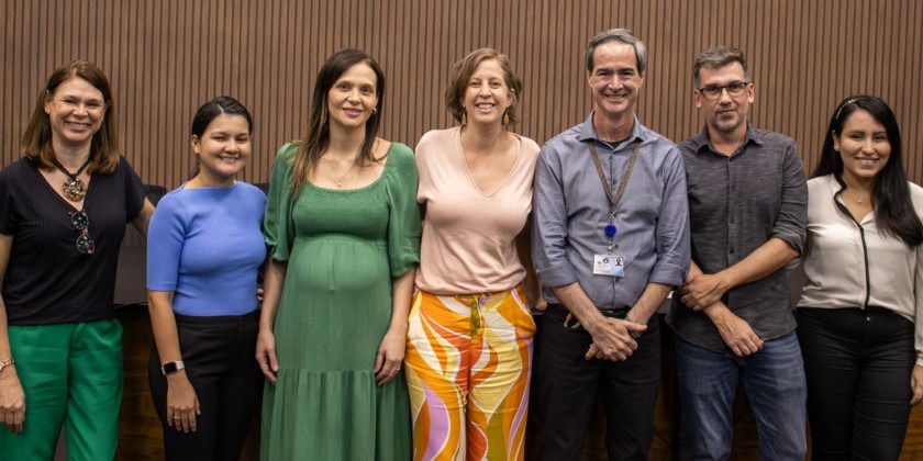 Fotografia colorida. Grupo de 7 pessoas posa para foto. São 5 mulheres e 2 homens. Fim da descrição.