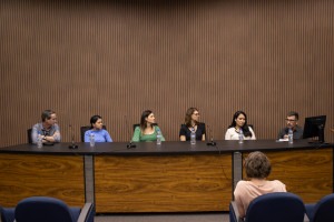 Fotografia colorida em ambiente interno. Seis pessoas estão sentadas em uma mesa.