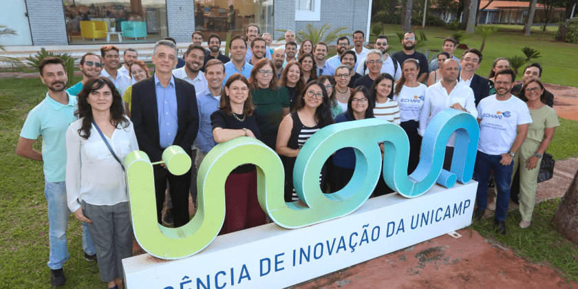 Na imagem, membros de empresas-filhas, incubadas e da equipe da inova posam para a foto em frente a placa na sede da Inova Unicamp