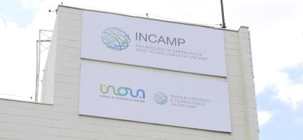 Placa com logo da Incamp no topo do prédio da Incubadora. Abaixo da placa da Incamp está uma placa com os logos da Inova Unicamp e do Parque Científico e Tecnológico da Unicamp Fim da descrição.